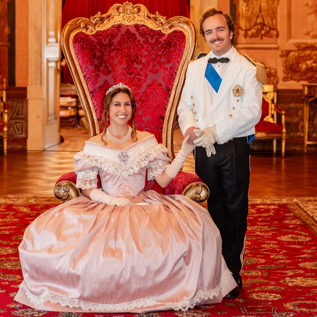 A Rainha sentada no trono ao lado do rei de pé